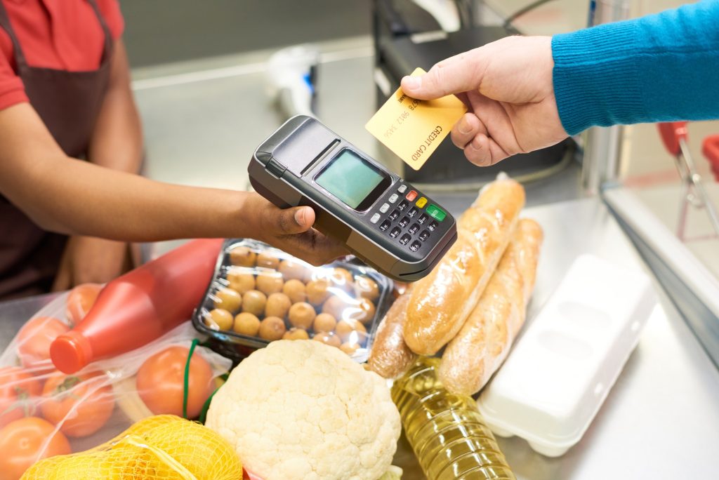 Male consumer holding credit card over payment terminal and food products